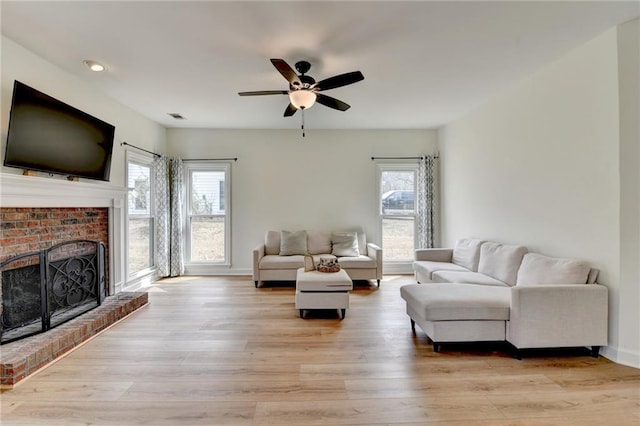 living area with visible vents, a fireplace, light wood-type flooring, and a ceiling fan