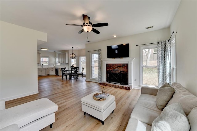 living room featuring baseboards, visible vents, a fireplace, ceiling fan, and light wood-type flooring