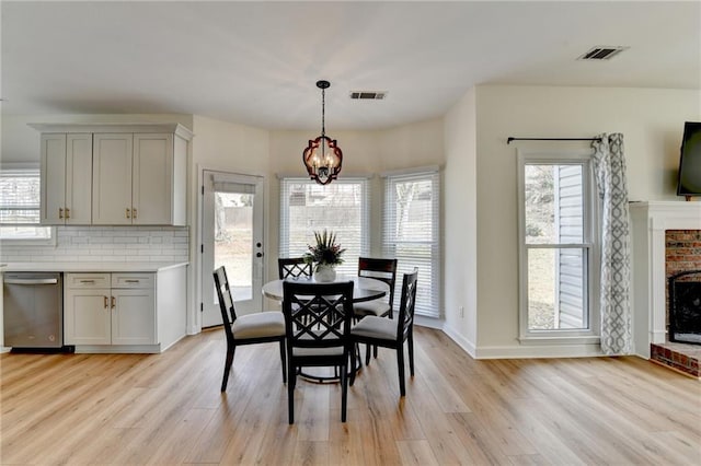 dining room with a brick fireplace, a notable chandelier, light wood-style flooring, and visible vents