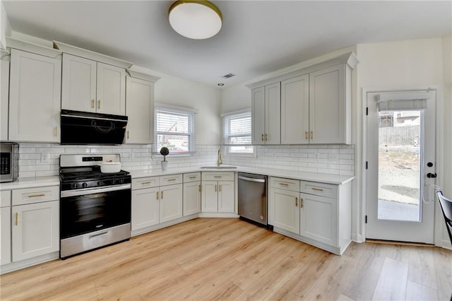 kitchen with a sink, decorative backsplash, light countertops, light wood-style floors, and appliances with stainless steel finishes