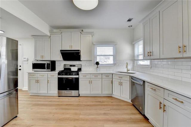 kitchen with light wood-style flooring, a sink, backsplash, stainless steel appliances, and light countertops