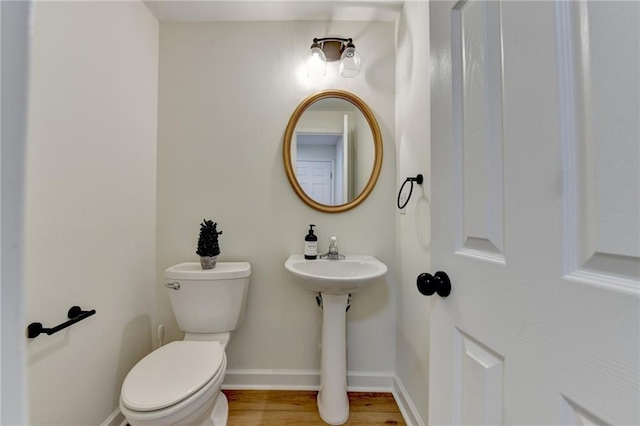 half bath featuring baseboards, toilet, and wood finished floors