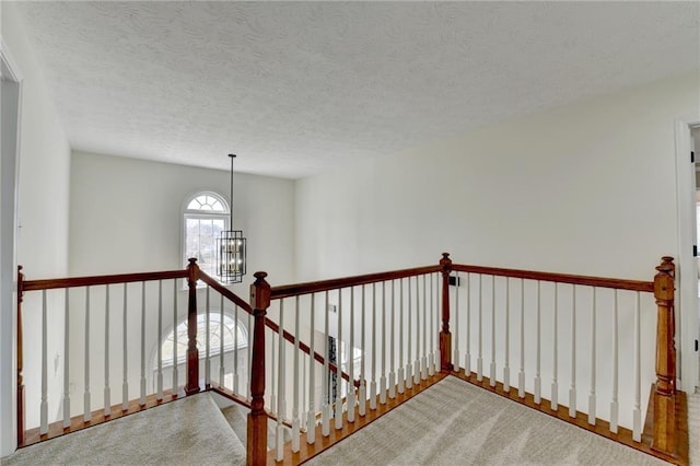 corridor featuring an upstairs landing, carpet flooring, a textured ceiling, and an inviting chandelier