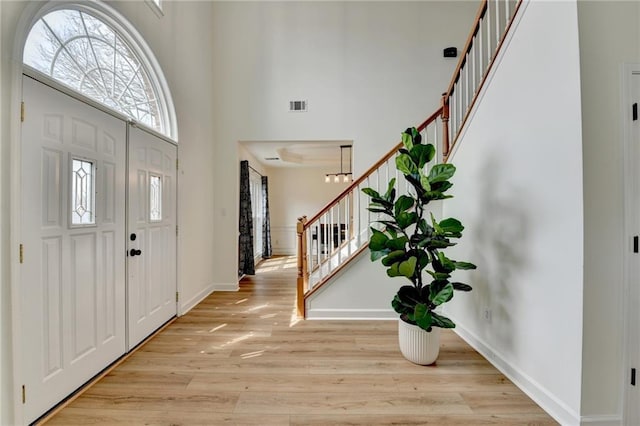 entryway with light wood-type flooring, visible vents, baseboards, a towering ceiling, and stairs