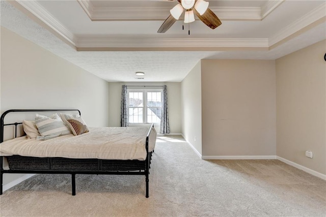 carpeted bedroom featuring a tray ceiling, baseboards, ornamental molding, and a ceiling fan