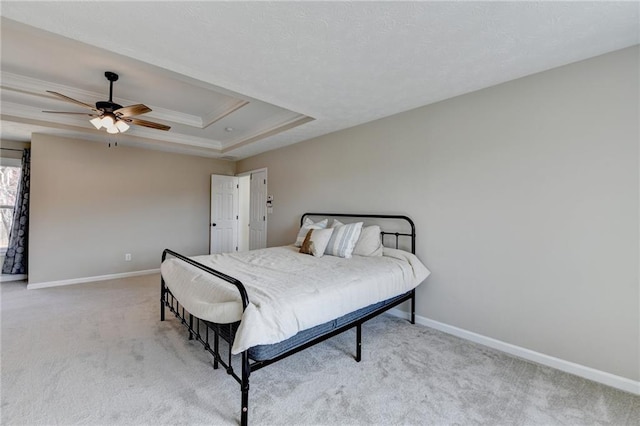 bedroom featuring crown molding, baseboards, ceiling fan, light colored carpet, and a tray ceiling