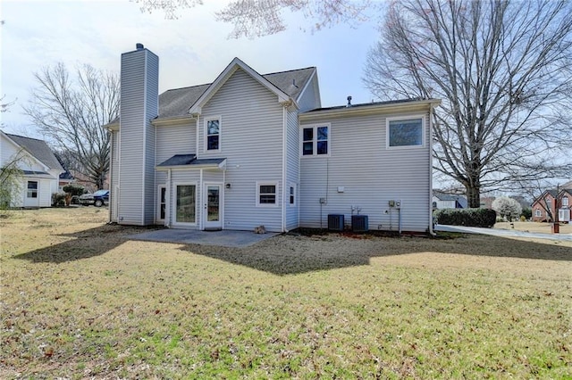 back of house featuring central air condition unit, a lawn, and a chimney