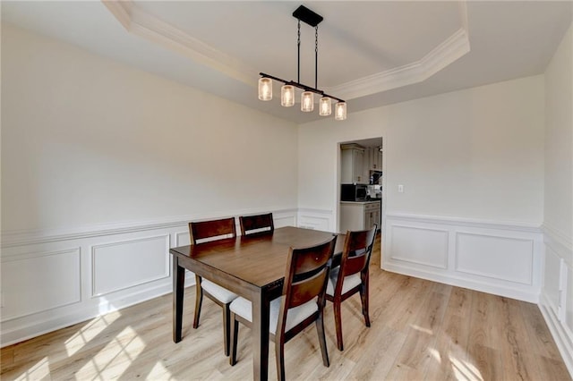 dining room with a wainscoted wall, ornamental molding, a tray ceiling, light wood-style floors, and a decorative wall