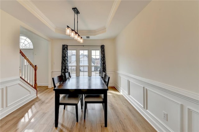 dining space with ornamental molding, stairs, light wood-style floors, a raised ceiling, and a decorative wall