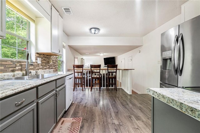 kitchen featuring stainless steel refrigerator with ice dispenser, gray cabinetry, a sink, dark wood-style flooring, and light countertops