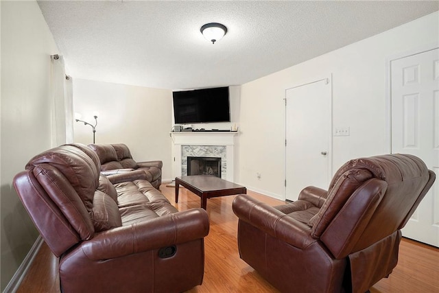 living area with light wood-style flooring, a tiled fireplace, a textured ceiling, and baseboards
