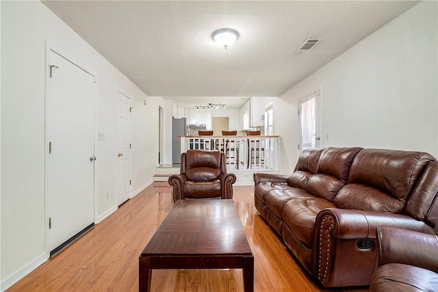 living area featuring light wood-style floors, a textured ceiling, track lighting, and baseboards