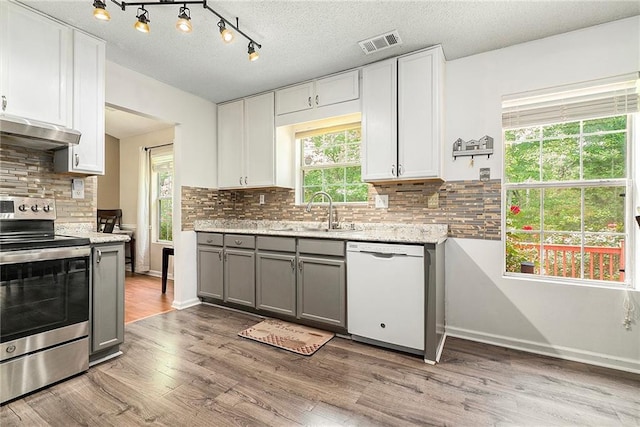 kitchen with white dishwasher, stainless steel electric range oven, a sink, under cabinet range hood, and gray cabinetry