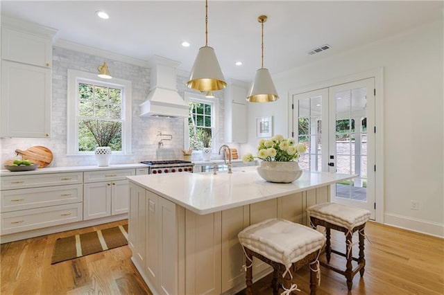 kitchen featuring visible vents, custom exhaust hood, light wood-style floors, french doors, and white cabinetry
