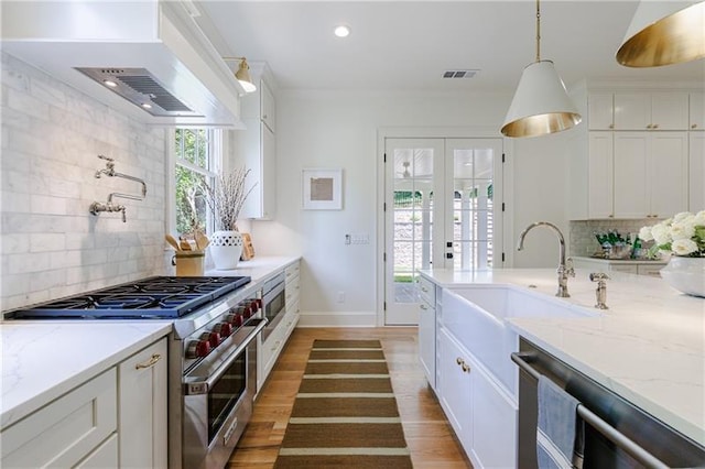 kitchen with premium range hood, light wood-style flooring, appliances with stainless steel finishes, white cabinetry, and a sink
