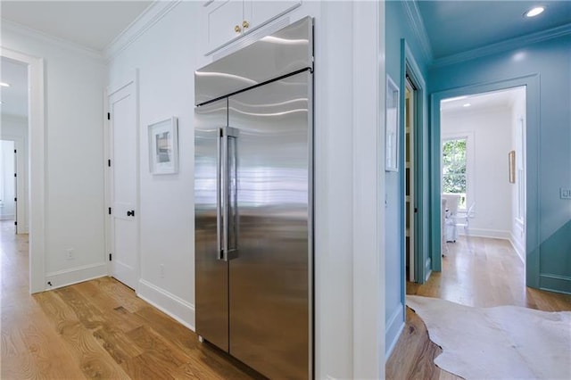 kitchen featuring light wood-type flooring, ornamental molding, built in fridge, white cabinets, and baseboards