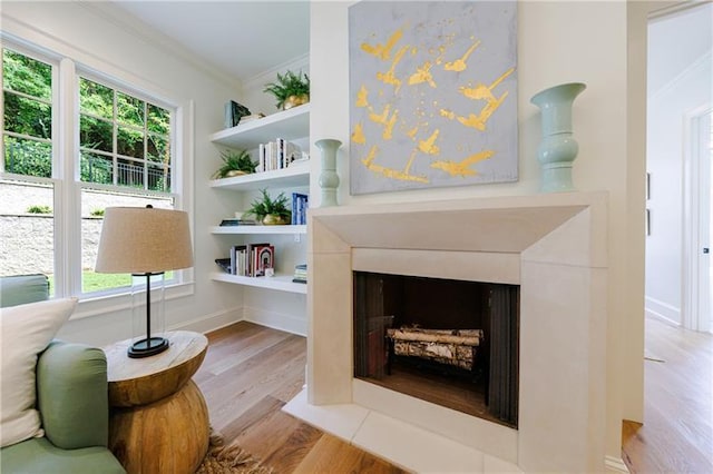 sitting room featuring plenty of natural light, wood finished floors, a fireplace with flush hearth, and ornamental molding