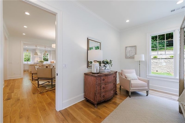 sitting room featuring crown molding, light wood-style flooring, baseboards, and a wealth of natural light