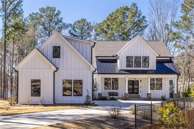 modern farmhouse style home with metal roof, a fenced front yard, a shingled roof, board and batten siding, and a standing seam roof