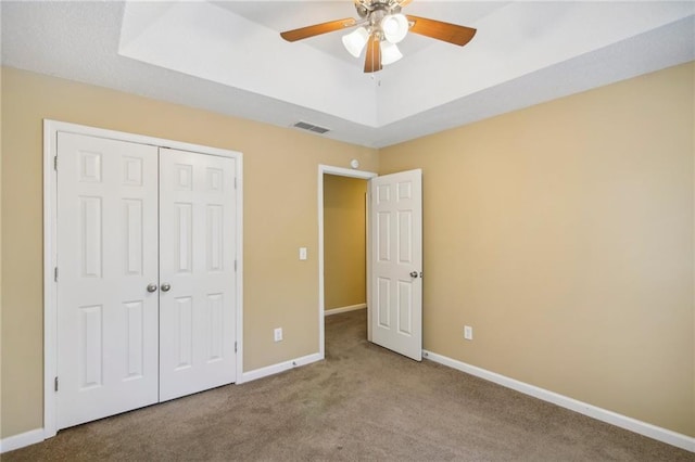 unfurnished bedroom featuring ceiling fan, a closet, a tray ceiling, and light carpet