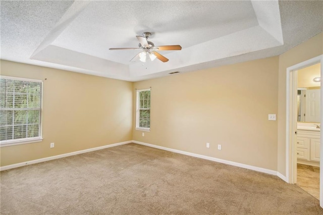 carpeted spare room with ceiling fan, plenty of natural light, a tray ceiling, and a textured ceiling