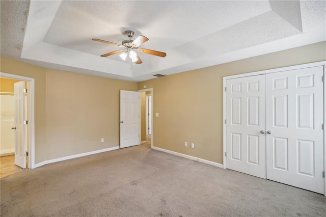 unfurnished bedroom featuring light carpet, a tray ceiling, a closet, and ceiling fan