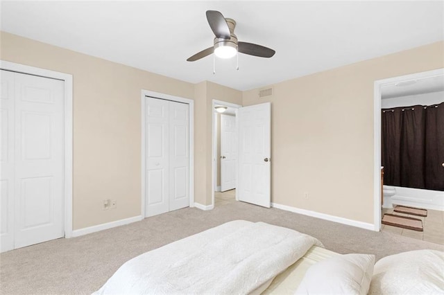 carpeted bedroom featuring connected bathroom, two closets, and ceiling fan