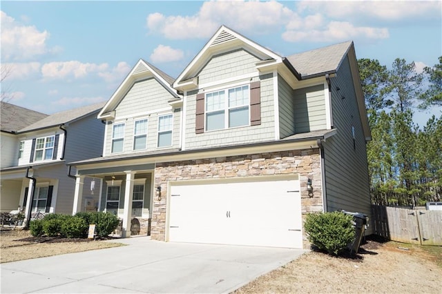 craftsman-style house featuring an attached garage, covered porch, fence, stone siding, and driveway