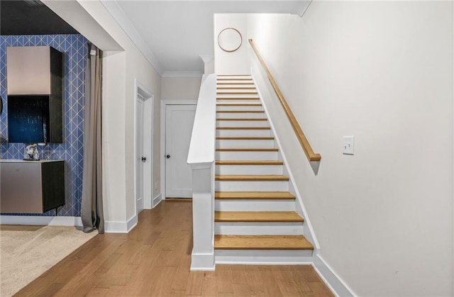 stairs with baseboards, wood finished floors, and crown molding