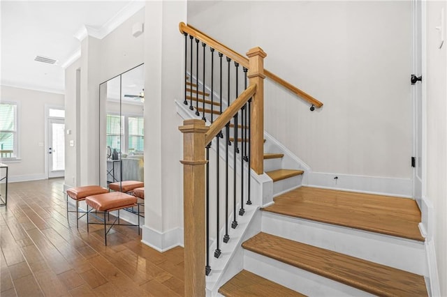 stairway with ornamental molding, plenty of natural light, wood finished floors, and baseboards