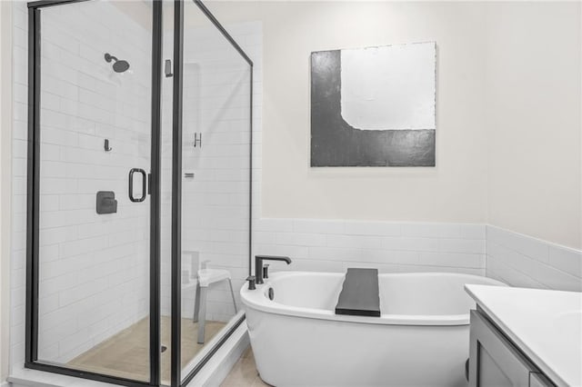 full bathroom with a shower stall, a freestanding bath, vanity, tile walls, and a wainscoted wall