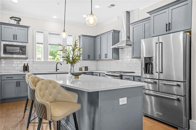kitchen featuring stainless steel appliances, wall chimney exhaust hood, gray cabinets, a sink, and crown molding