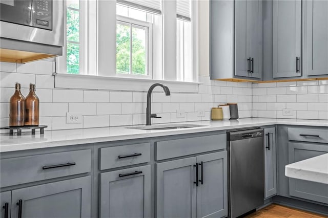 kitchen with gray cabinetry, stainless steel appliances, a sink, decorative backsplash, and light stone counters