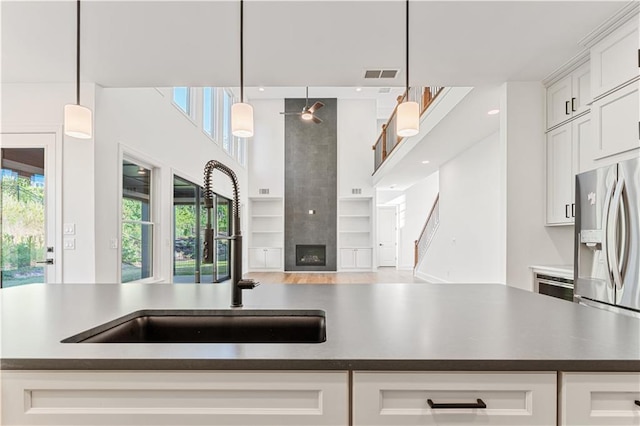 kitchen with white cabinets, a high end fireplace, decorative light fixtures, a center island with sink, and stainless steel fridge with ice dispenser