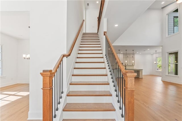 staircase featuring a towering ceiling, a healthy amount of sunlight, and wood-type flooring