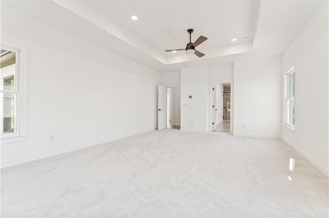 empty room featuring light carpet, a raised ceiling, and ceiling fan