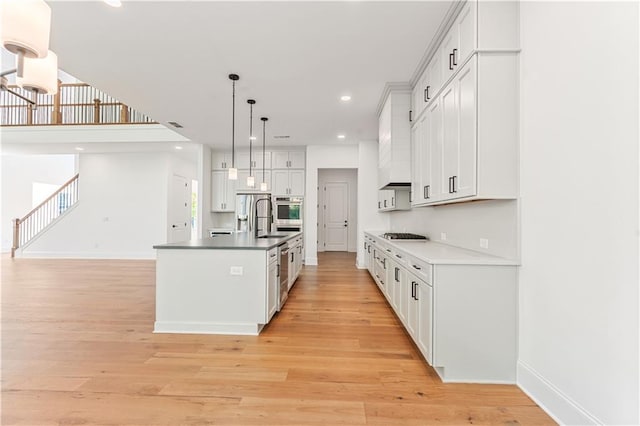 kitchen with white cabinetry, a center island with sink, decorative light fixtures, and light hardwood / wood-style floors