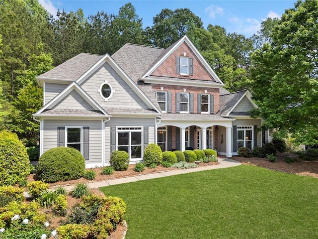 view of front of property with covered porch, a shingled roof, and a front yard