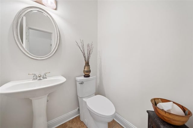 half bathroom with baseboards, a sink, and toilet