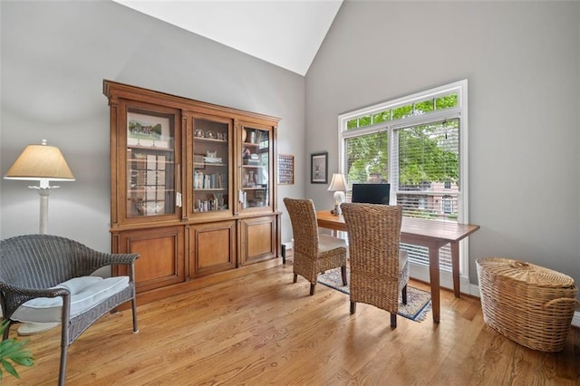 office space with high vaulted ceiling, baseboards, and light wood-style flooring