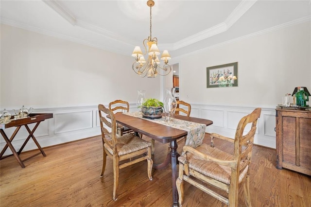 dining area featuring crown molding, wainscoting, a notable chandelier, light wood-style floors, and a tray ceiling