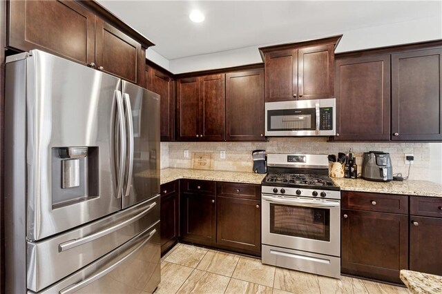 kitchen featuring decorative backsplash, light stone countertops, dark brown cabinetry, and appliances with stainless steel finishes