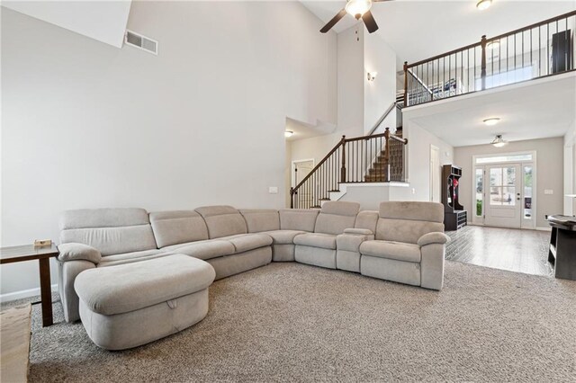 carpeted living room featuring ceiling fan and a towering ceiling