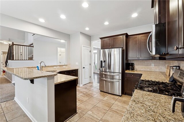 kitchen featuring light stone countertops, appliances with stainless steel finishes, decorative backsplash, a kitchen breakfast bar, and sink