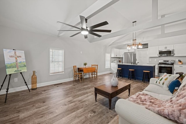 living area featuring vaulted ceiling with beams, baseboards, ceiling fan with notable chandelier, and wood finished floors