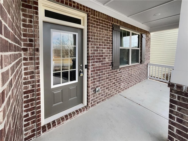 doorway to property featuring covered porch and brick siding