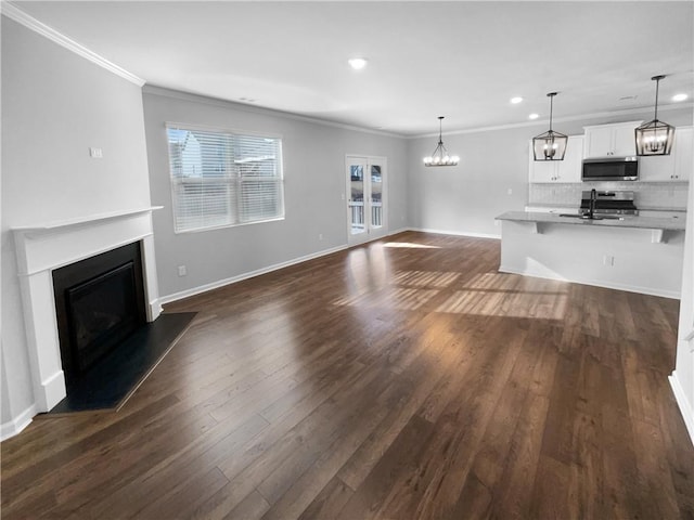 unfurnished living room featuring ornamental molding, a fireplace, dark wood finished floors, and an inviting chandelier