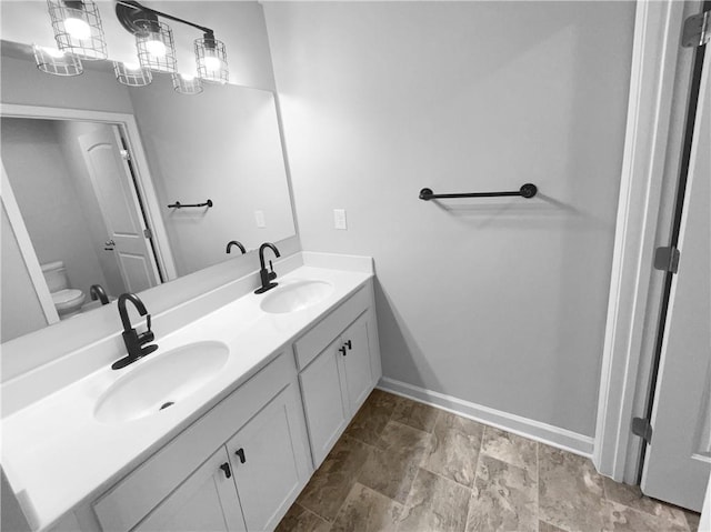 bathroom with toilet, double vanity, baseboards, and a sink