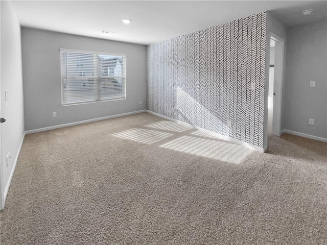 empty room with an accent wall, baseboards, and carpet flooring