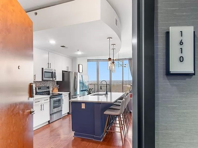 kitchen with appliances with stainless steel finishes, white cabinetry, a sink, and wood finished floors